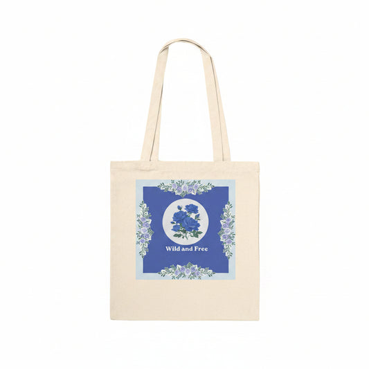A natural canvas tote bag with a blue and white floral graphic on the front, featuring the text 'Wild and Free' and two shoulder straps, shown against a plain white background.